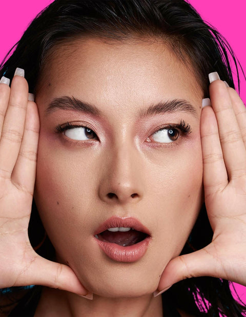 Model showcasing EYE LIGHT eyeshadow stick with pink background.