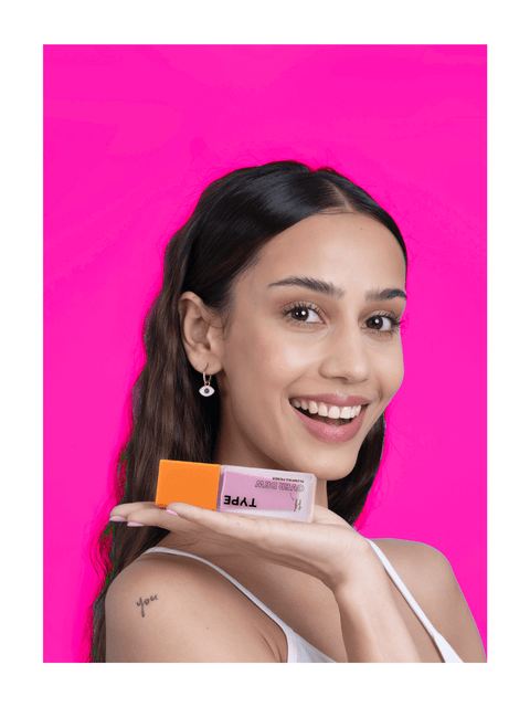 "Smiling woman showcasing primer sample set on pink background."