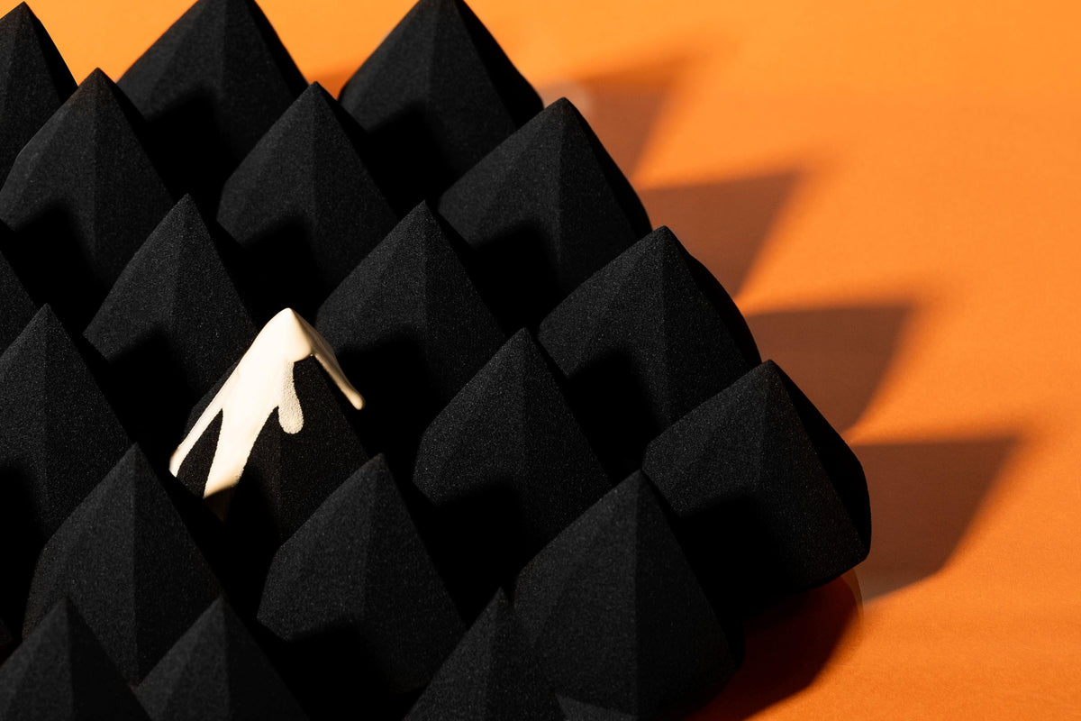 Black pyramid sponge with cream droplet on orange background.