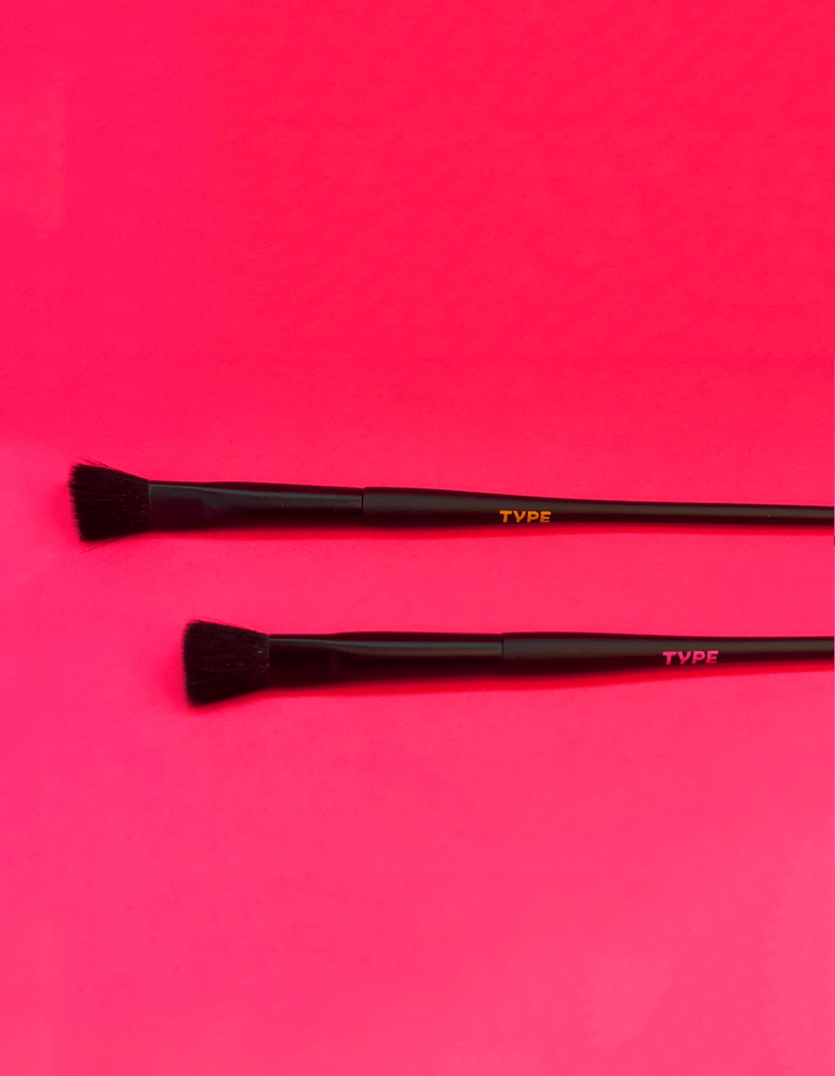 Black makeup brushes on a vibrant pink background for science-themed beauty products.