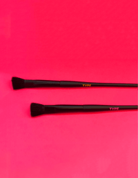 Black makeup brushes on a vibrant pink background for science-themed beauty products.